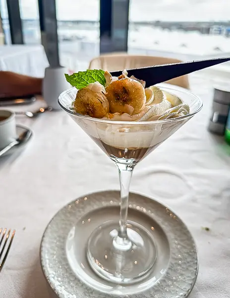 A sweet dessert featuring bananas, caramel, and cream, elegantly presented in a martini glass.