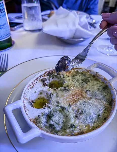 A close-up of escargot baked in garlic and herb butter, served in a classic white dish.