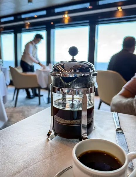 A steaming pot of freshly brewed French press coffee served in the Haven restaurant with an ocean view in the background.