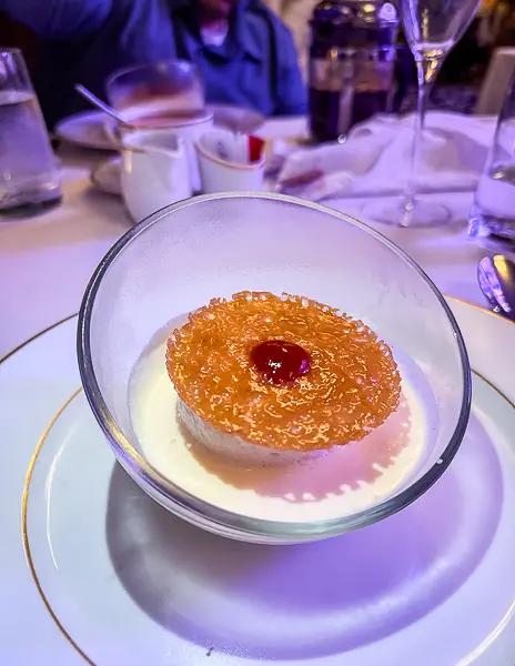 A delicate Île Flottante dessert topped with a caramelized sugar disk and a cherry.