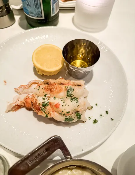 A perfectly cooked lobster tail garnished with parsley, served with a wedge of lemon and melted butter.