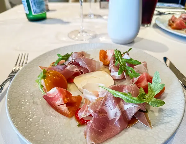 A colorful plate of fresh mozzarella surrounded by thinly sliced prosciutto, cherry tomatoes, and arugula, captured during lunch at The Haven on Norwegian Getaway.