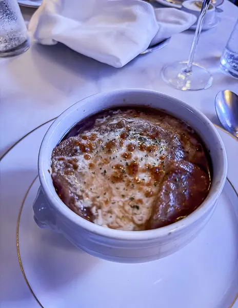 A comforting bowl of French onion soup topped with melted cheese, served in an elegant dining setting.