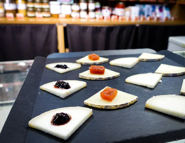 A selection of Spanish cheeses topped with fruit preserves, neatly arranged on a black slate serving board at a Girona food market.