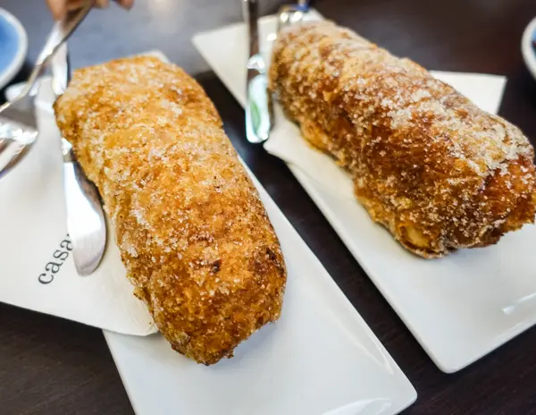 Two xuixo pastries on white plates at Casamoner in Girona, Spain. These flaky, sugar-coated pastries are filled with Catalan cream and are a must-try local specialty.