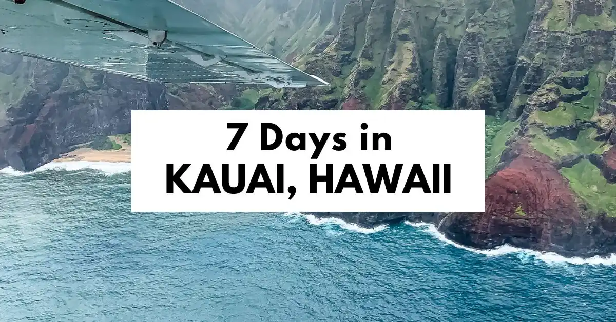 featured blog image of a wide aerial view of Kauai’s rugged coastline, with a wing of a plane visible in the frame and a bold text overlay that reads "7 Days in KAUAI, HAWAII". The ocean waves crash against the dramatic cliffs and secluded beaches below.