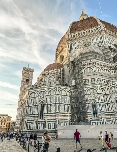 Exterior view of the Duomo di Firenze (Florence Cathedral) at golden hour, with people walking nearby.