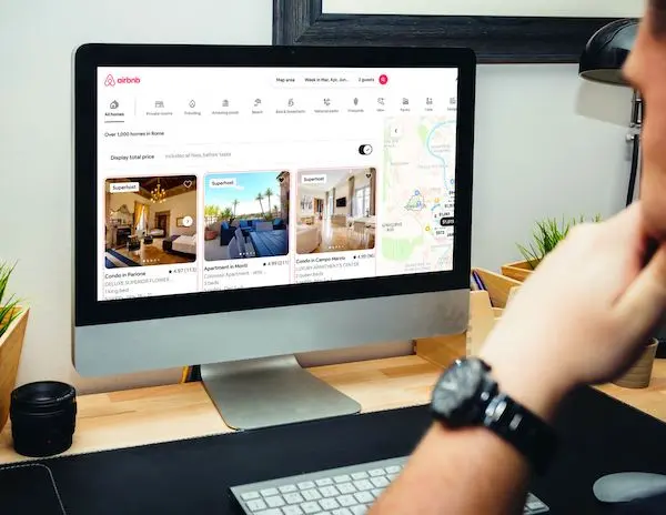 Person browsing Airbnb listings on a desktop computer, with various properties displayed on the screen.