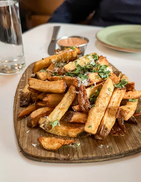 A wooden board heaped with Belgian fries, sprinkled with herbs and grated cheese at magnolia house in pasadena