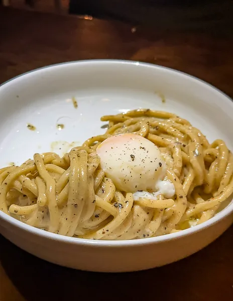 A bowl of cacio e pepe pasta topped with a poached egg, freshly cracked black pepper sprinkled on top at union pasadena