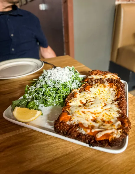 A plate with a chicken parmesan dish served with a side salad.