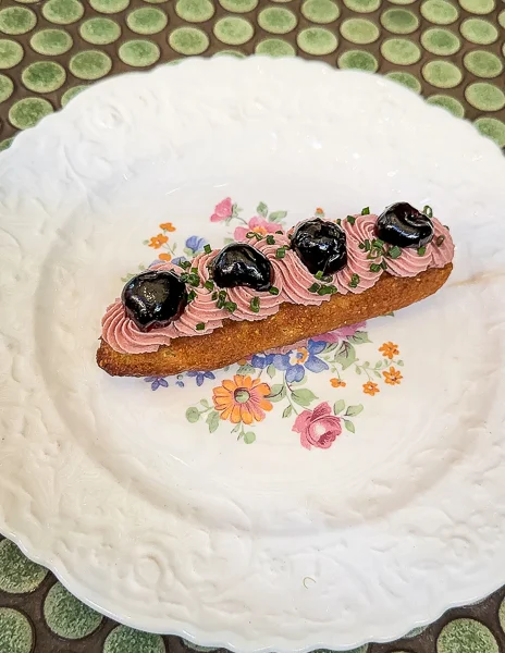 A cornbed éclair topped with liver mouse and black cherries on a floral-patterned plate at agnes pasadena