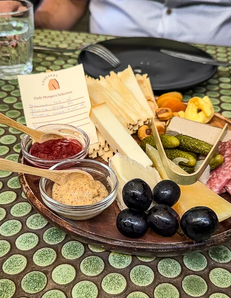 A charcuterie board featuring a selection of cheeses, meats, pickles, and accompaniments, with a menu card on a patterned tabletop at agnes pasadena