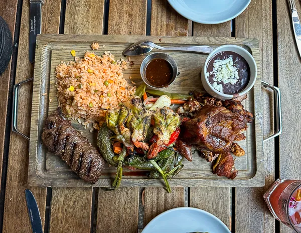 A wooden platter with a variety of grilled meats, rice, and sauces