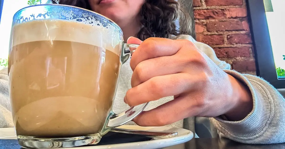 Close-up of a latte in a clear glass mug, held by a person (kathy) sitting in one of the cozy cafes and coffee shops in Pasadena, California.