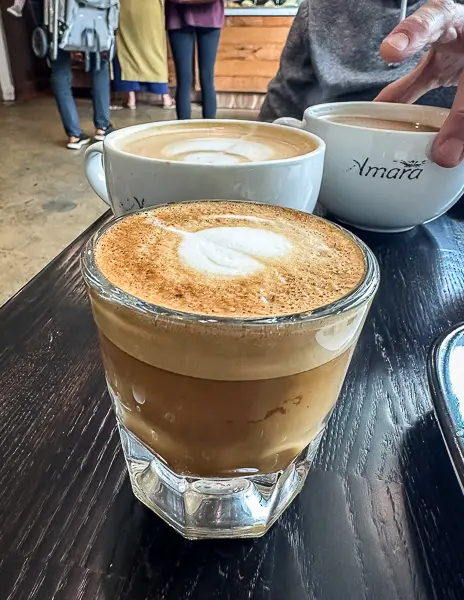 A close-up of a cortadito and lattes served in branded mugs at Amara Café in Pasadena, with a cozy café interior in the background.