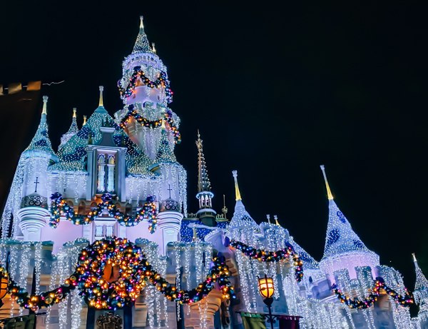 Sleeping Beauty Castle beautifully decorated with garlands, colorful ornaments, and twinkling Christmas lights at Disneyland during the holidays.