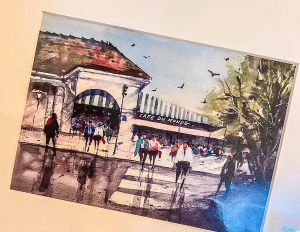 Watercolor painting of Café du Monde in New Orleans, depicting people walking past the iconic beignet shop.