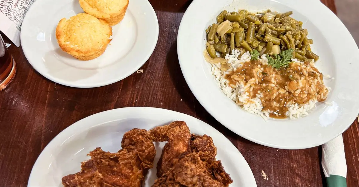 featured blog image image displays a meal with crispy fried chicken, green beans over rice with shrimp gumbo, and cornbread muffins, set on a wooden table, highlighting popular dishes at places to eat in New Orleans.