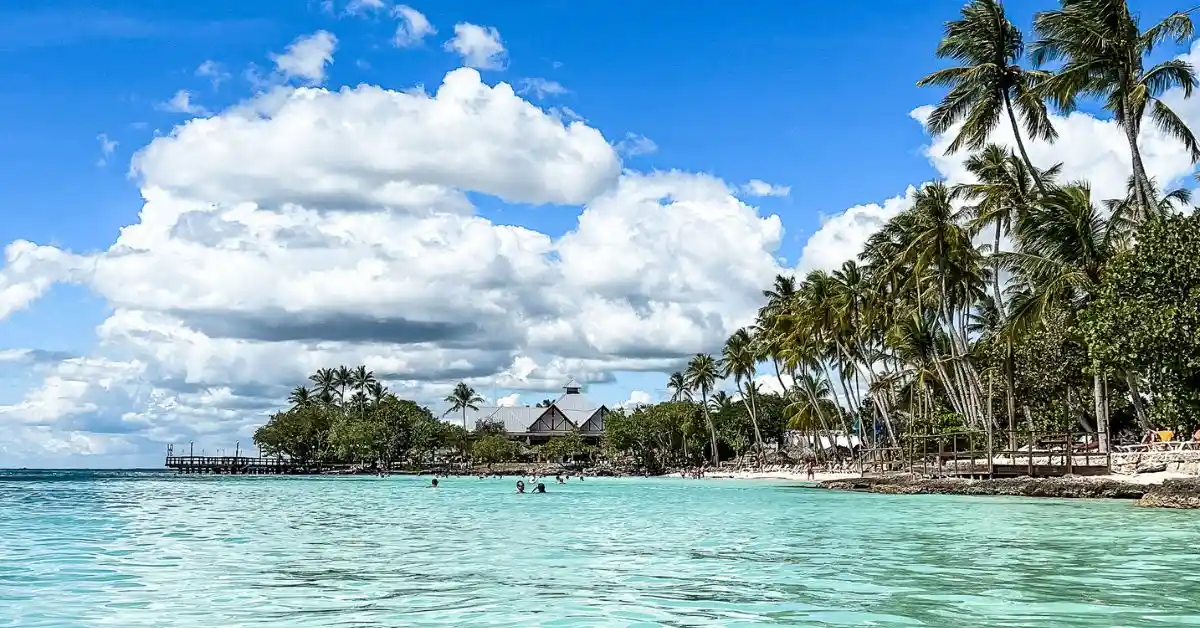 Featured blog image of idyllic view of Hilton La Romana Resort on Playa Bayahibe, featuring a lush landscape of palm trees along a pristine beach, with a traditional pier extending into the crystal-clear turquoise waters under a sky dotted with fluffy clouds.