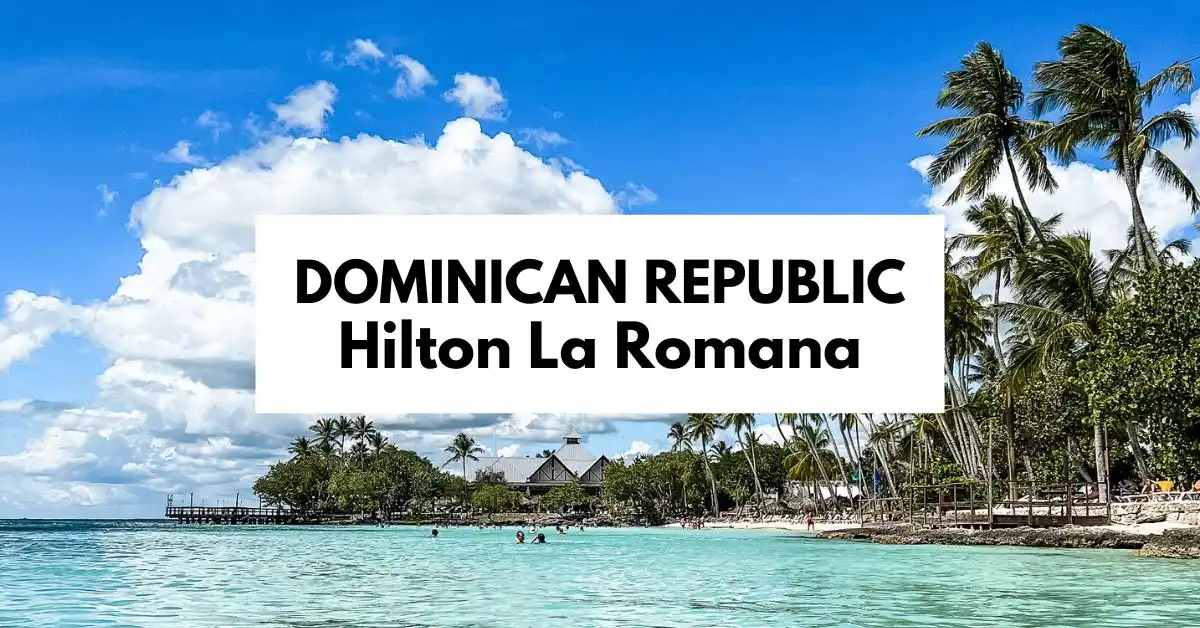 featured blog image of a view of Hilton La Romana resort along Playa Bayahibe in the Dominican Republic, showcasing a tropical beach with palm trees, clear turquoise waters, and a traditional wooden pier under a sunny sky with fluffy clouds.