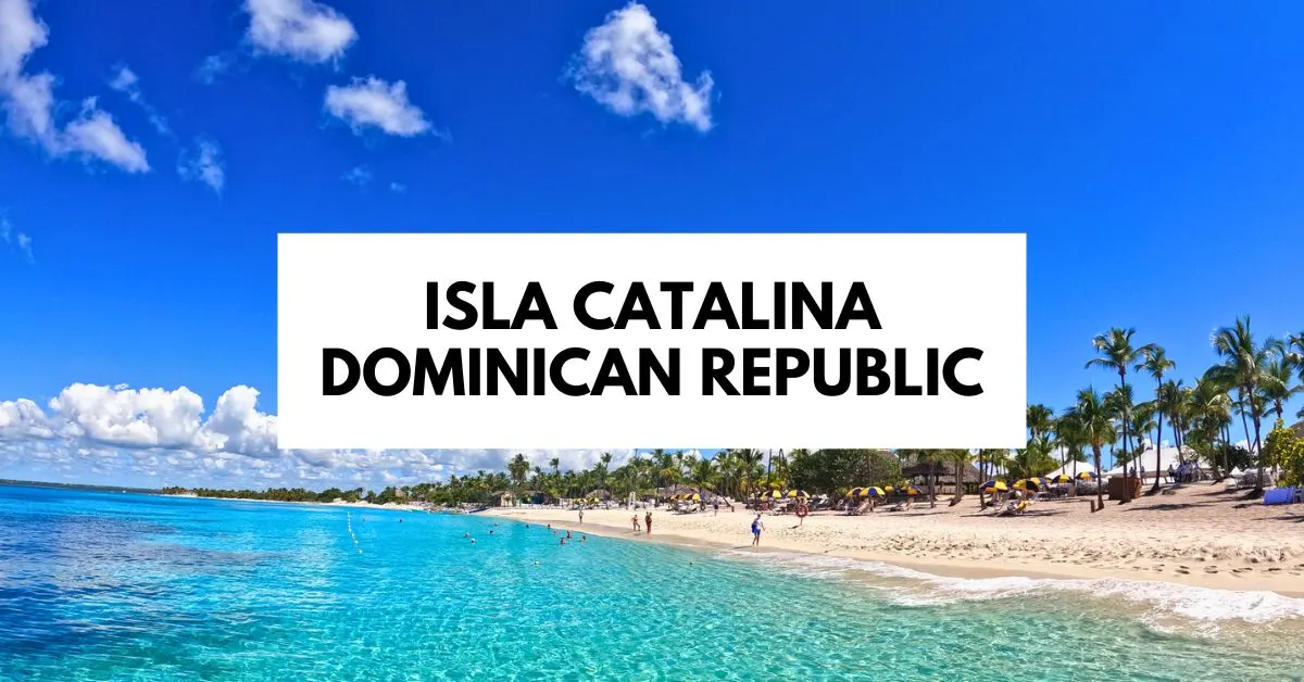 A beautiful beach on Isla Catalina, Dominican Republic, with clear blue water, white sand, and people relaxing under palm trees and umbrellas.