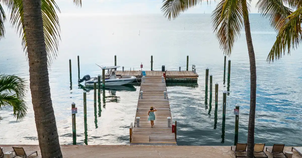 featured image: A tranquil scene, highlighting things to do in Islamorada, Florida, with a woman walking down a wooden pier framed by palm trees and overlooking the calm, clear waters of the Florida Keys.