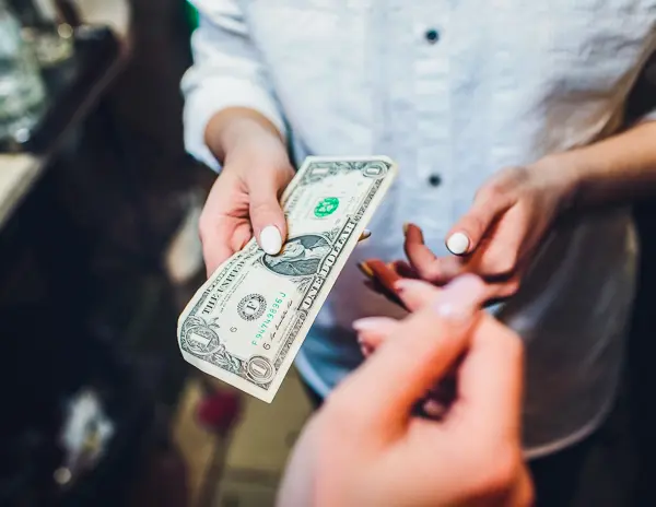 a close-up view of a financial transaction, with one person handing over a dollar bill to another person, likely as a tip for services rendered.