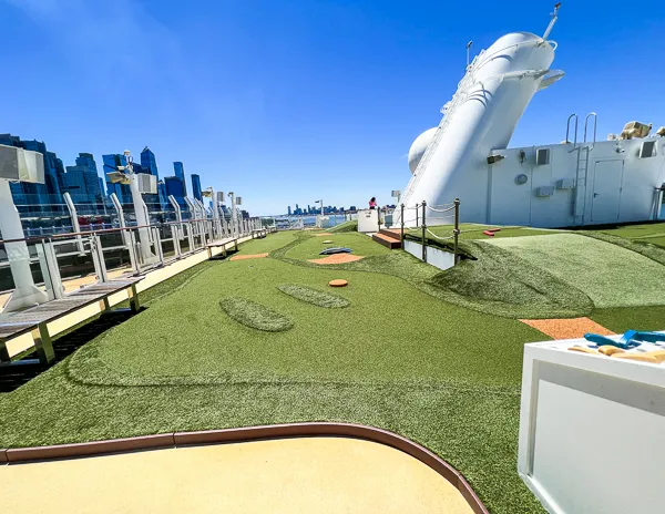 Mini golf course on the deck of a cruise ship with a city skyline in the background.