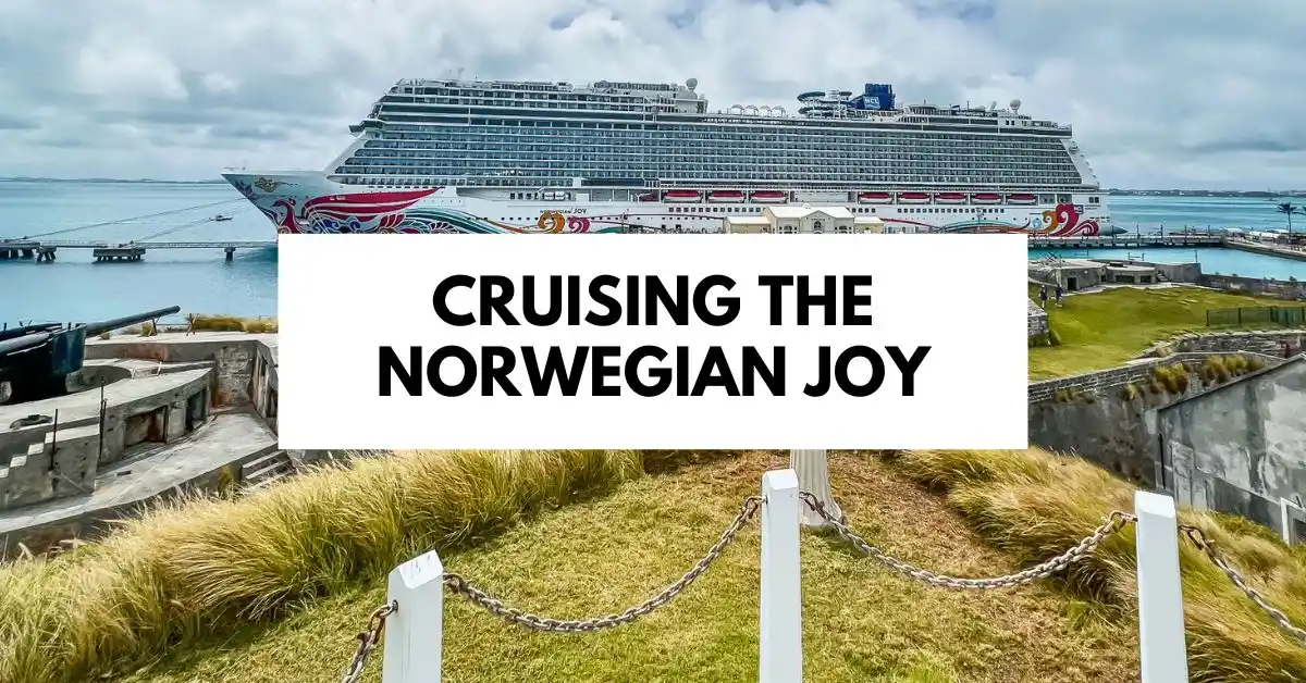 Norwegian Joy cruise ship docked in Bermuda, surrounded by greenery and historic fortifications, with bold text overlay reading 'Cruising the Norwegian Joy.'