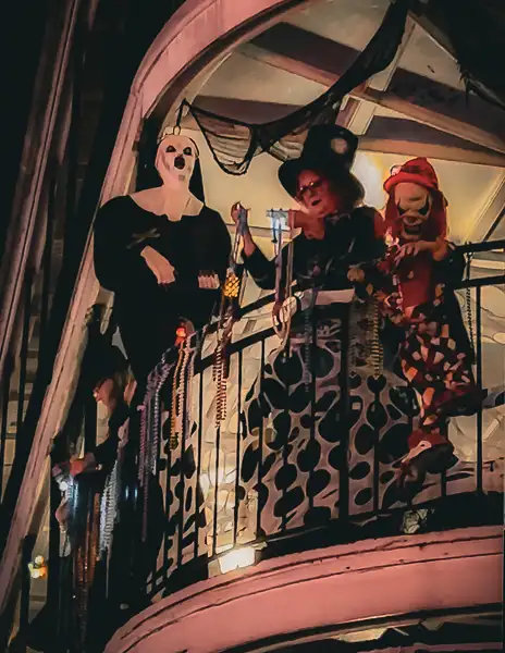 A woman in a Halloween costume holding Mardi Gras beads on a decorated balcony in New Orleans, surrounded by spooky decorations