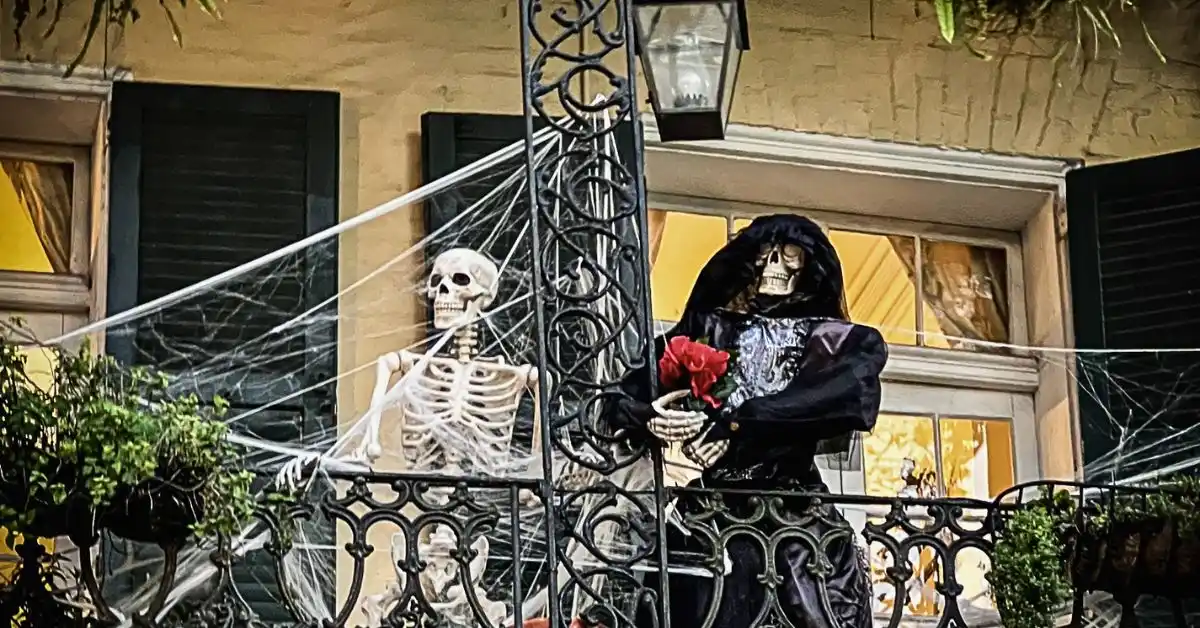 Featured blog image showing skeletons dressed in Halloween costumes on a balcony with cobwebs and ironwork in the French Quarter during halloween in new orleans.