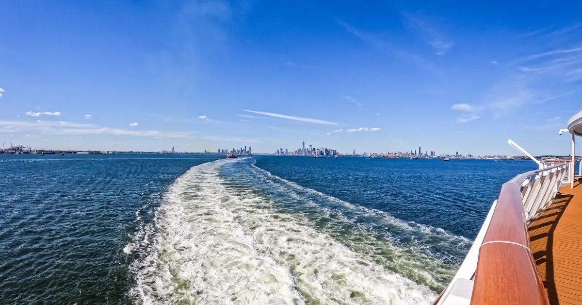 featured blog image of a view from a cruise ship deck showing the ocean and city skyline in the distance, highlighting the pros and cons of cruises.