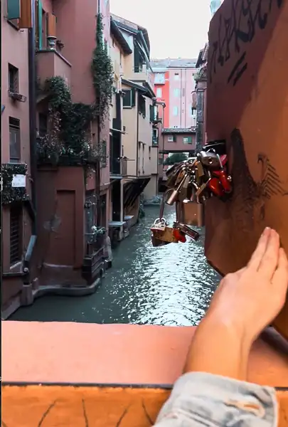 A person (kathy) opening the Little Window on Via Piella in Bologna to reveal a hidden canal, with padlocks visible in the foreground.