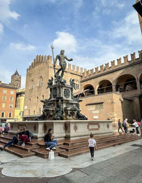 Neptune’s Fountain in Piazza Maggiore, surrounded by people enjoying the lively square, with historic brick buildings in the background.