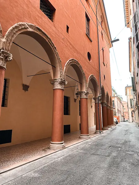 A quiet street in Bologna flanked by endless porticoes with red and cream-colored columns and arches.