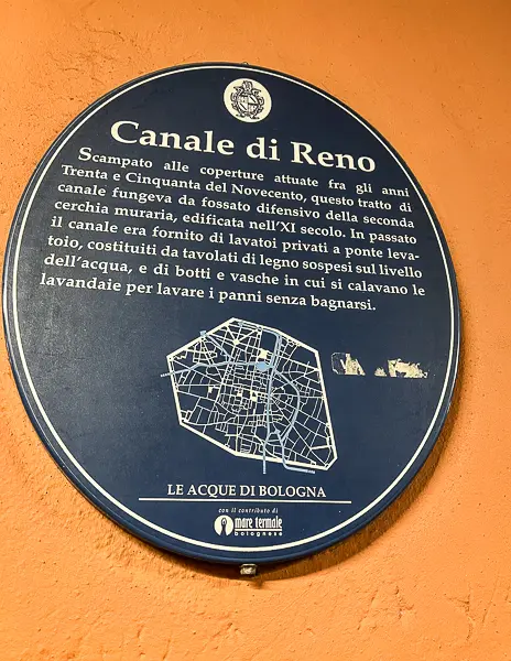 A close-up of the Canale di Reno sign in Bologna, Italy, detailing the history of the canal system against an orange wall.