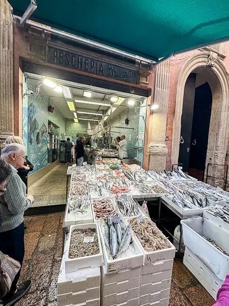 A fish market in Bologna's Quadrilatero district, featuring crates of fresh seafood displayed outside Pescheria Brunelli.