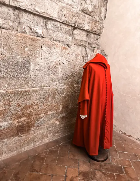 A vibrant red 12th-century robe displayed during the secret passages tour at Palazzo Vecchio in Florence, illustrating the historical clothing of the era.