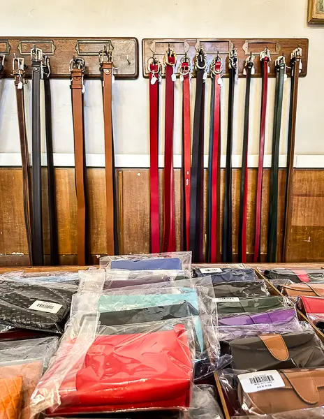 A selection of handcrafted leather belts hanging on display and colorful wallets packaged and arranged at the Leather School of Florence (Scuola del Cuoio).