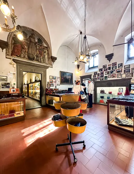 Inside the Leather School of Florence (Scuola del Cuoio), featuring a beautifully lit room with historical decor, leather goods on display, and staff assisting visitors.