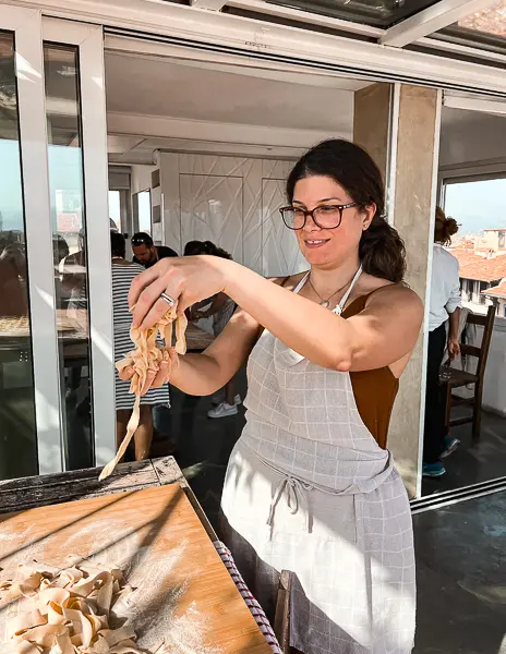 A woman (kathy) in an apron holding fresh pasta she made during a cooking class in Florence, with a bright and airy kitchen setting.