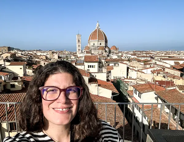 A woman (kathy) taking a selfie with a breathtaking view of Florence, including the Duomo and the city’s rooftops, on a sunny day.