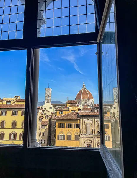 A stunning view of the Florence Duomo framed by a large window during the Secret Passages Tour at Palazzo Vecchio, showcasing the historic skyline of Florence under a clear blue sky.