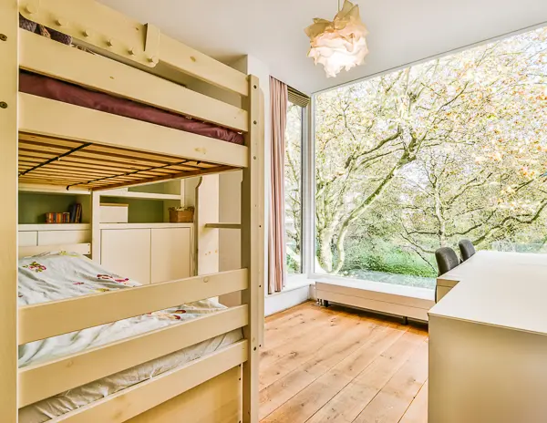 a cozy, well-lit bedroom with wooden bunk beds, a large window providing a stunning view of lush greenery, and a wooden floor.