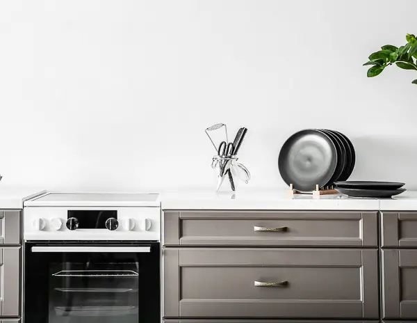 a modern kitchen with sleek, gray cabinetry and a clean, minimalistic design. The countertop is white, holding a set of black plates stacked neatly and a knife holder with various kitchen utensils. 