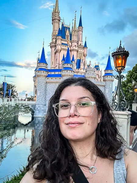 kathy smiling in front of Cinderella Castle at Disney World, with the castle's iconic spires and blue rooftops under a cloudy sky.