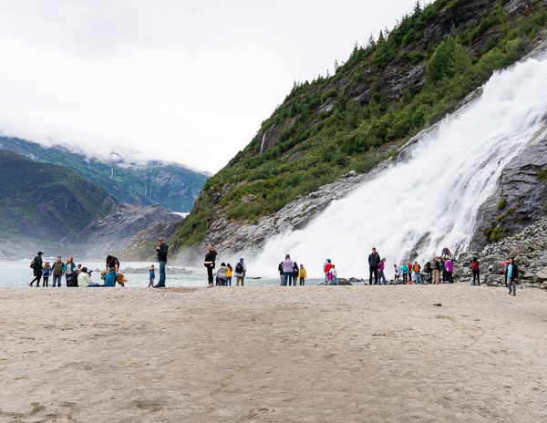 Visitors gathered at Nugget Falls, enjoying the powerful waterfall and the scenic surroundings with the glacier in the backdrop.