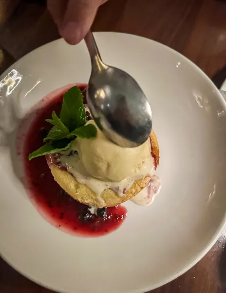 A plate of butter cake topped with vanilla ice cream and berry compote, a spoon poised to dive in at nicks pasadena