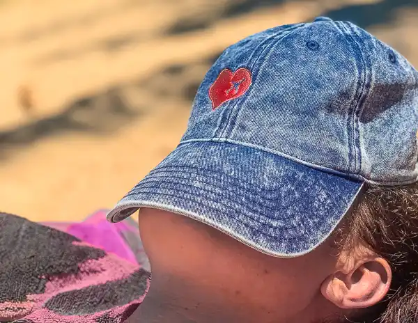 kathy wearing a faded blue denim cap with a red heart embroidered on it, using it for shade on a sunny day.